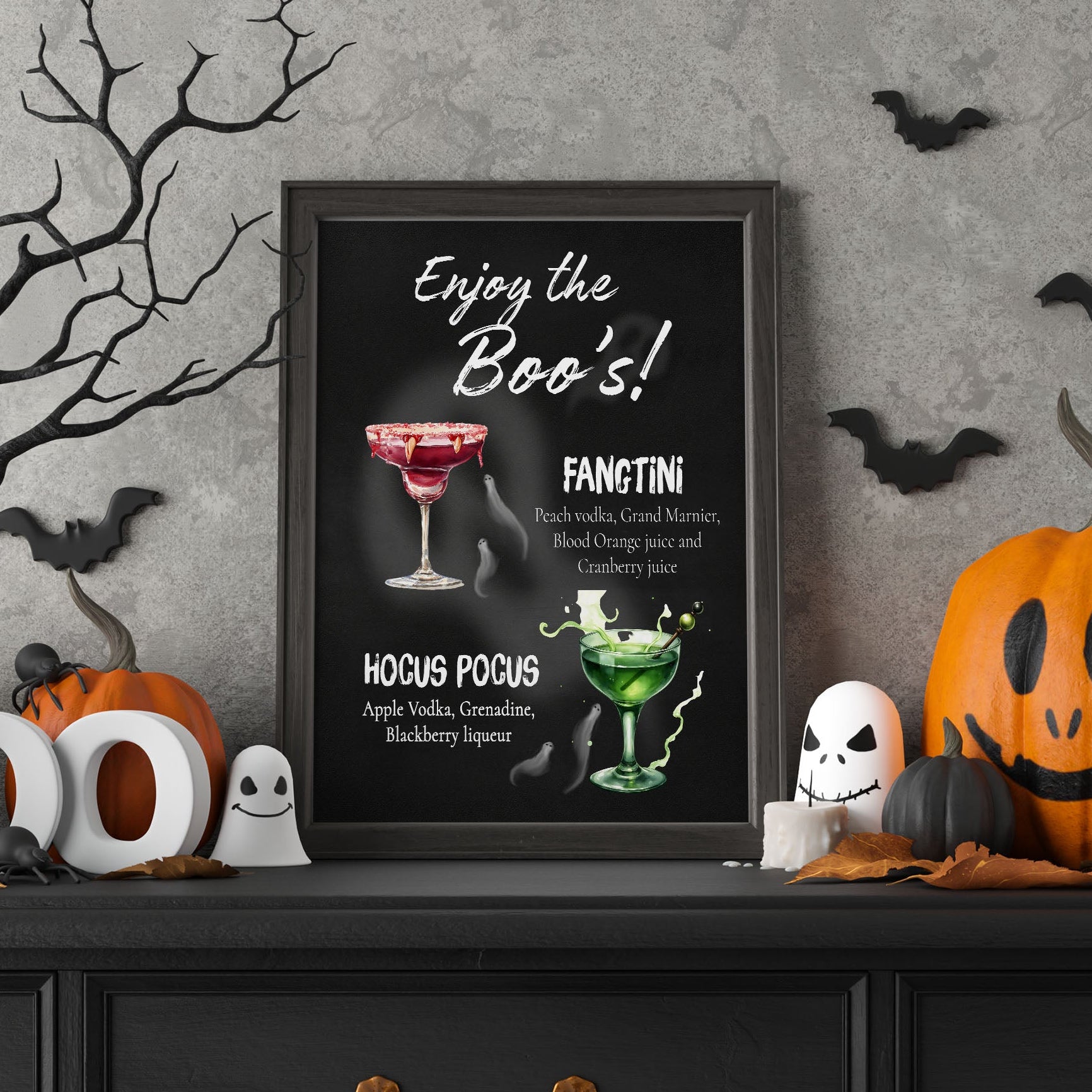 A framed Halloween-themed cocktail recipe poster reading 'Enjoy the Boo's!' and 'Fangtini' is displayed on a dark wooden cabinet. The scene is decorated with orange pumpkins, a carved pumpkin, white ghost figures, a bare tree branch, and black bat cutouts against a textured gray wall.