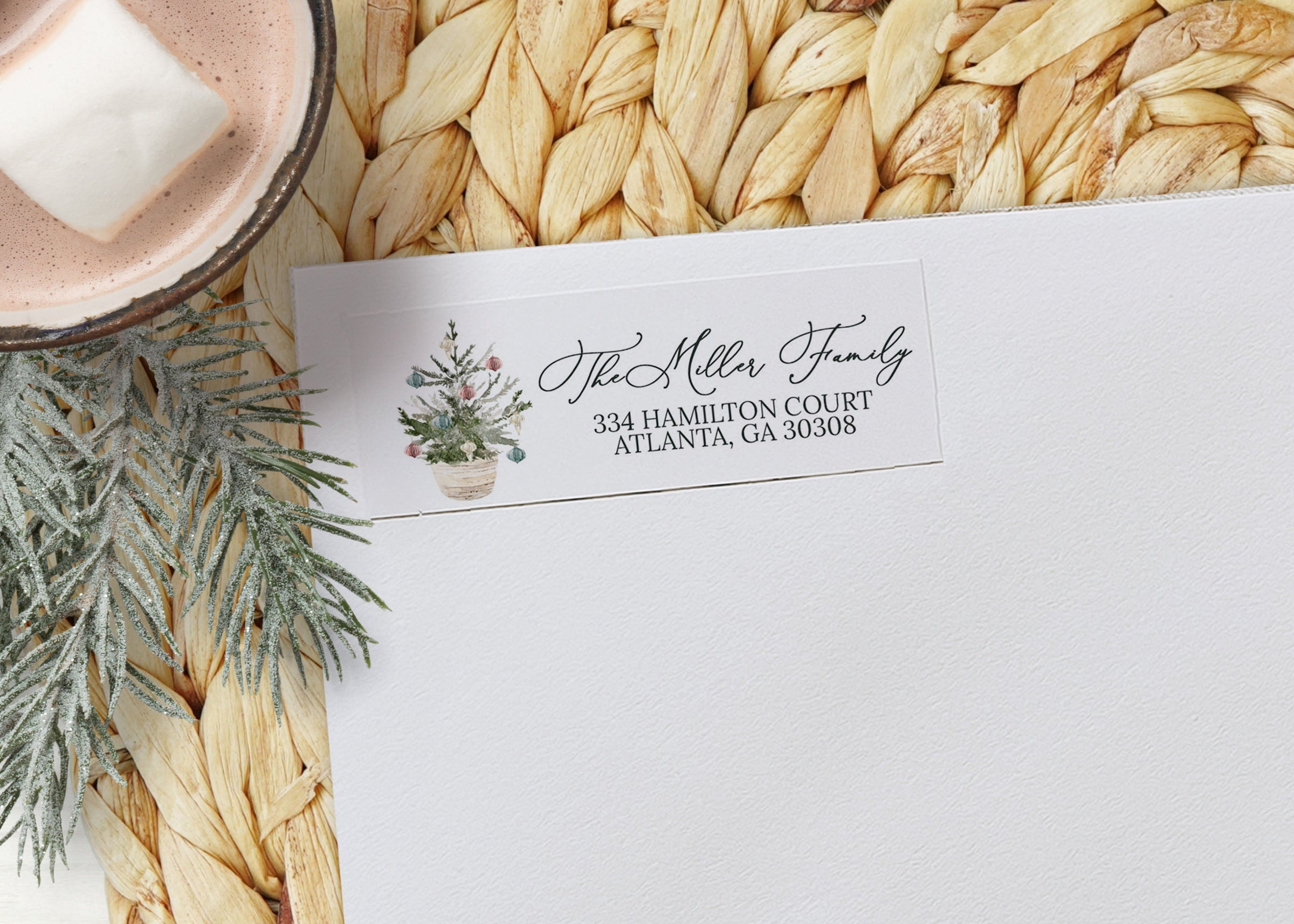 White envelope with personalized address label on a woven mat with hot chocolate and marshmallows.