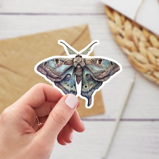 Hand holding a butterfly-shaped sticker on a wooden surface with an envelope and basket.