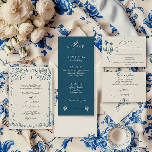 An elegant wedding invitation suite laid out on a table with blue floral patterns, including a save the date, invitation, RSVP, and information card, with a pocket fold on the side.