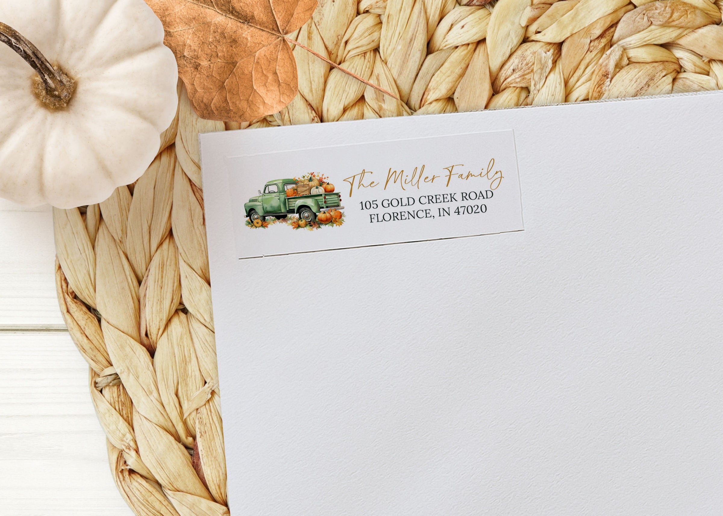 White envelope with fall-themed address label on a woven mat with pumpkins.