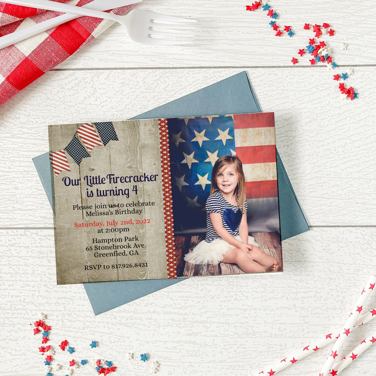 Invitation card with American flag design and photo of a child on a wooden surface with decorative items.