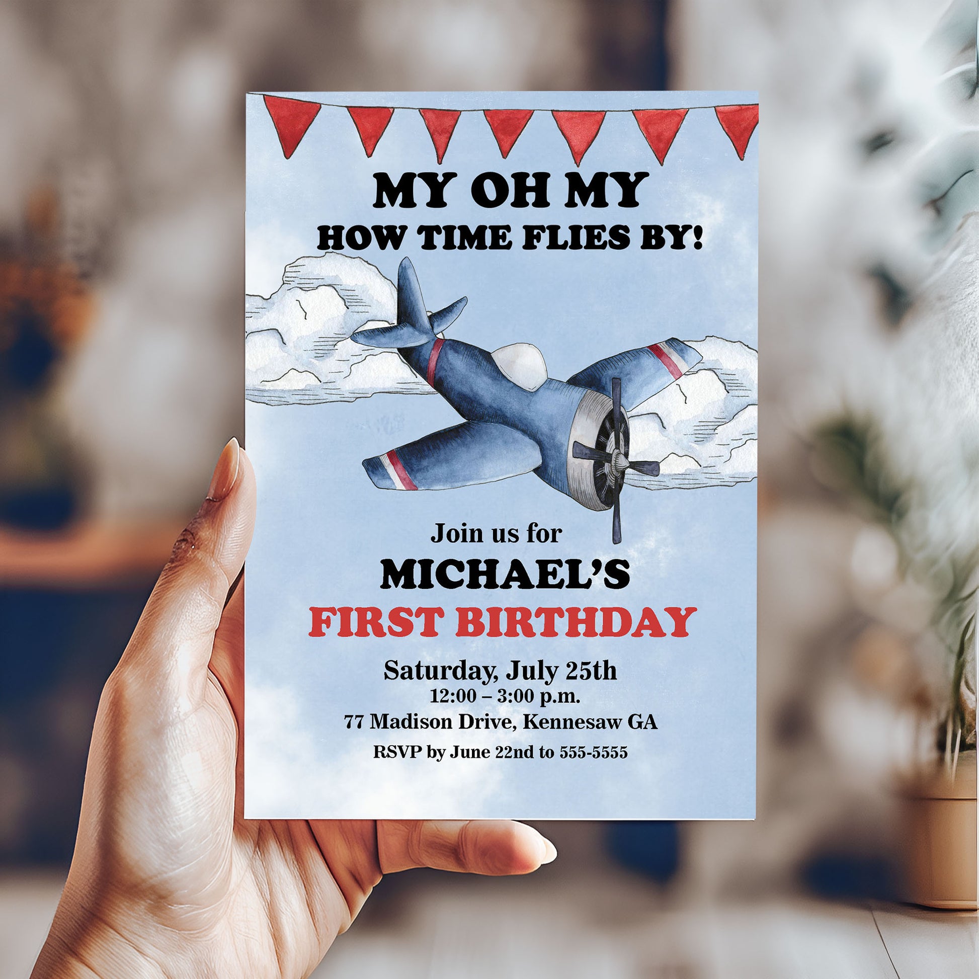 Hand holding a birthday invitation card with an airplane design and text.