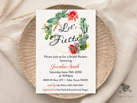 A bridal shower invitation with a floral design and the text 'Let's Fiesta' prominently displayed. The invitation is laid out on a woven table mat.