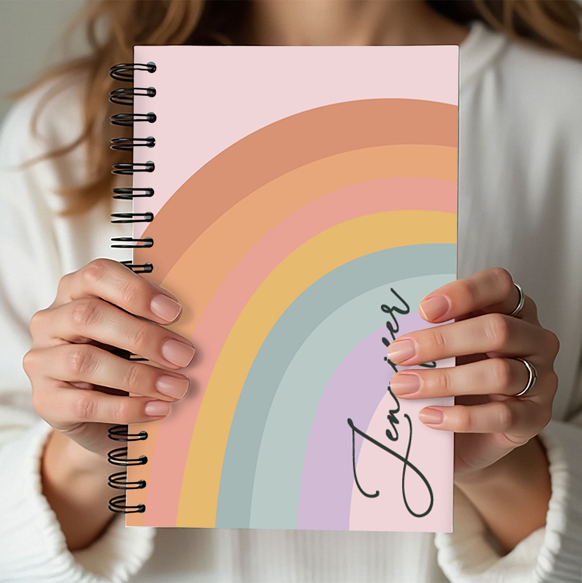 Person holding a notebook with a rainbow design and the word 'Journal' on the cover.